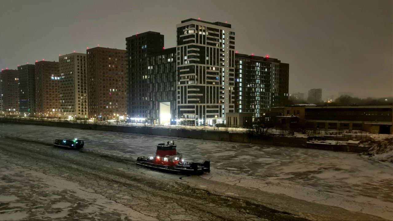 Зимняя Москва-река, сумрак раннего утра, сквозь лёд пробивается буксир, за ним в кильватере идёт речной трамвай.