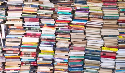 The image shows a wall of books stacked haphazardly, creating a visually stunning texture of various colors and sizes. The foreground is dominated by the densely packed books, while the background is mostly obscured by the sheer volume of literature. The location appears to be an outdoor book market, perhaps in a Spanish-speaking country, judging by some of the visible titles. The titles visible in the image show a mix of classic and contemporary literature, suggesting a wide diversity of literary preferences.