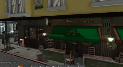 The image shows a virtual recreation of a street scene in Dublin, Ireland. In the foreground is a quaint pub named "The Blarney Stone", with a green awning and traditional Irish decor. The background includes other buildings, suggesting a bustling city atmosphere. There are cobblestone streets and various details like street lamps and hanging flower baskets, adding to the overall ambiance. A red vintage-style gas pump is visible near the curb, and a car can be spotted parked in the distance, adding a touch of realism to the virtual setting. The avatar's name, ‘Danie Timeless’, is visible on the screen, suggesting the use of a digital avatar in a virtual environment.