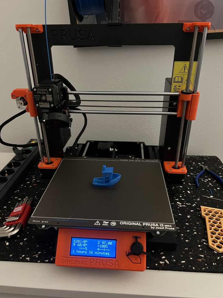 A photograph of a Prusa 3D printer displaying a finished print of a test model.