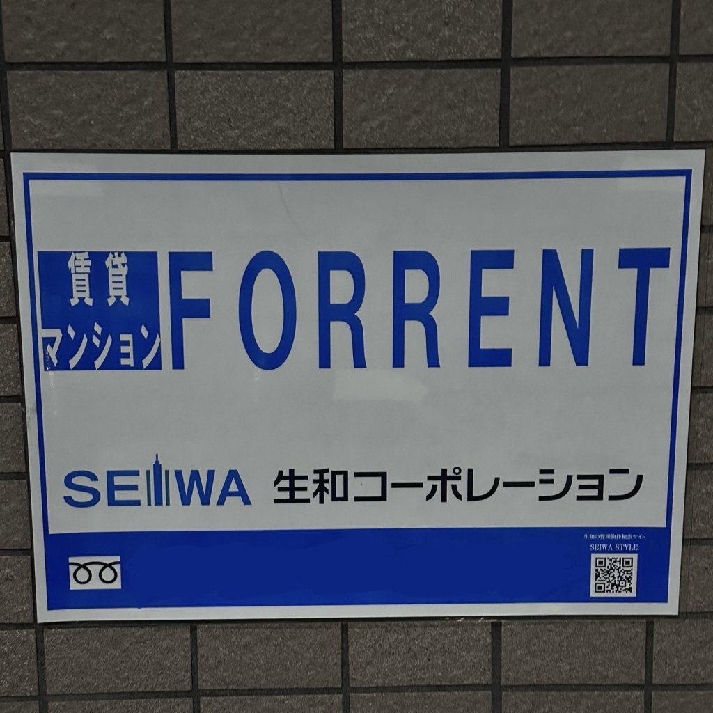 Blue and white "FOR RENT" sign with Japanese text and a QR code on a tiled wall.

The spacing of the English letters is inconsistent/weird