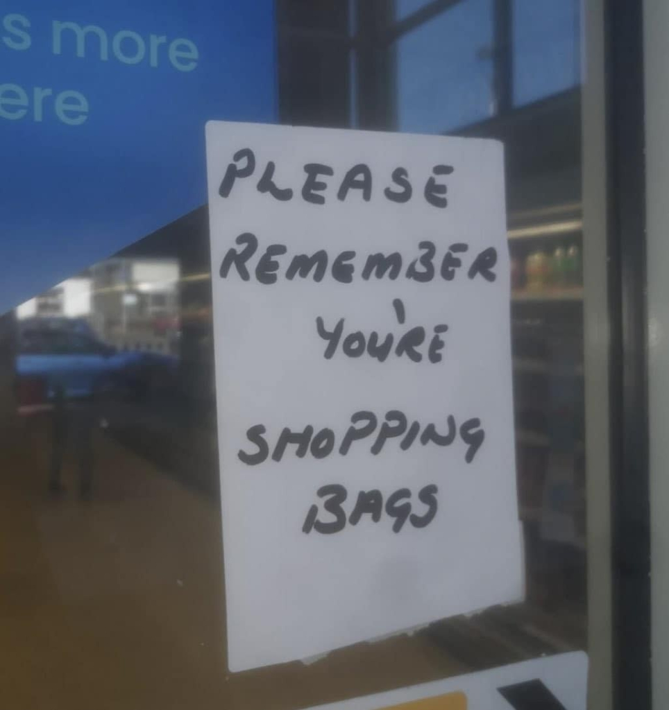 hand written sign on a door that says: "Please remember you're [sic] shopping bags."