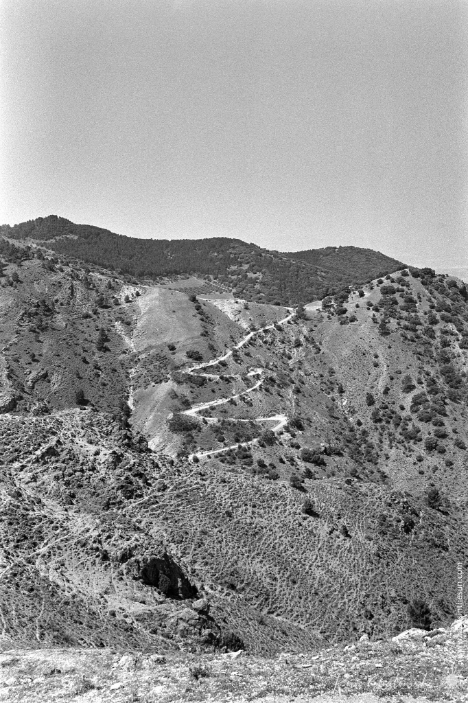 A black-and-white photo of a dirt track zig-zagging its way through the mountains.