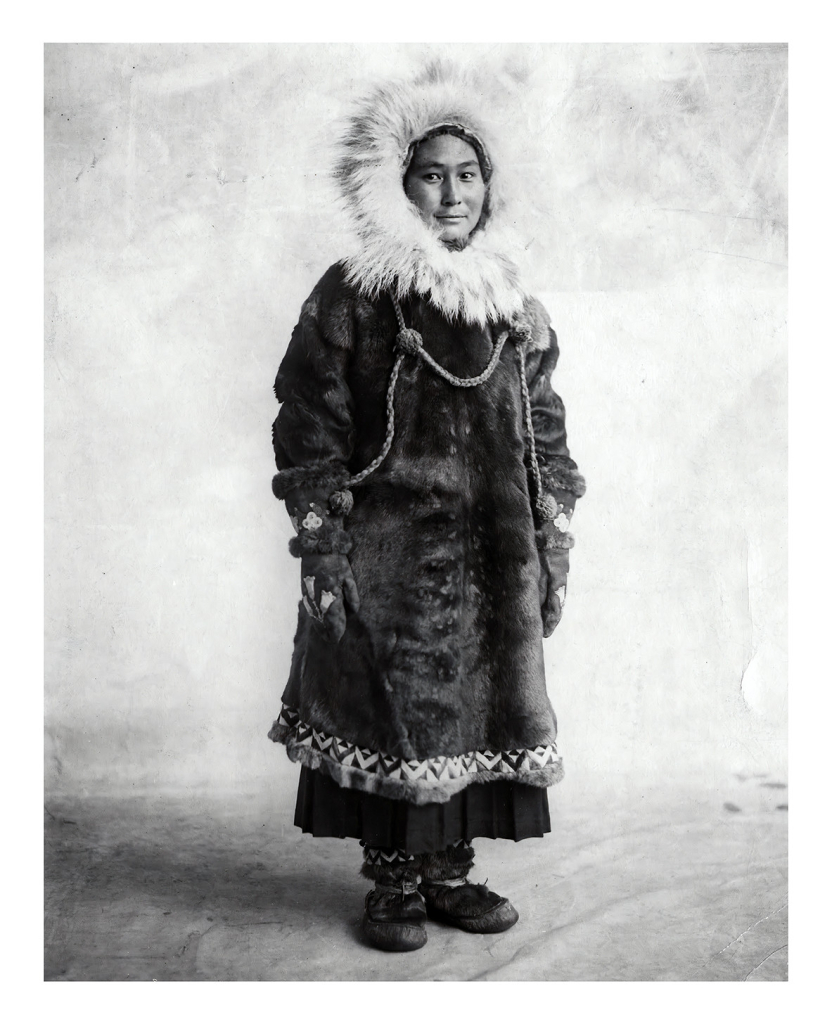 Black and white photo of Ada, a young Iñupiaq woman dressed in a traditional outfit with a fur hood.