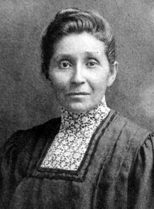 A black and white close photograph of Susan La Flesche, with her hair pinned up, wearing a high necked grey dress.