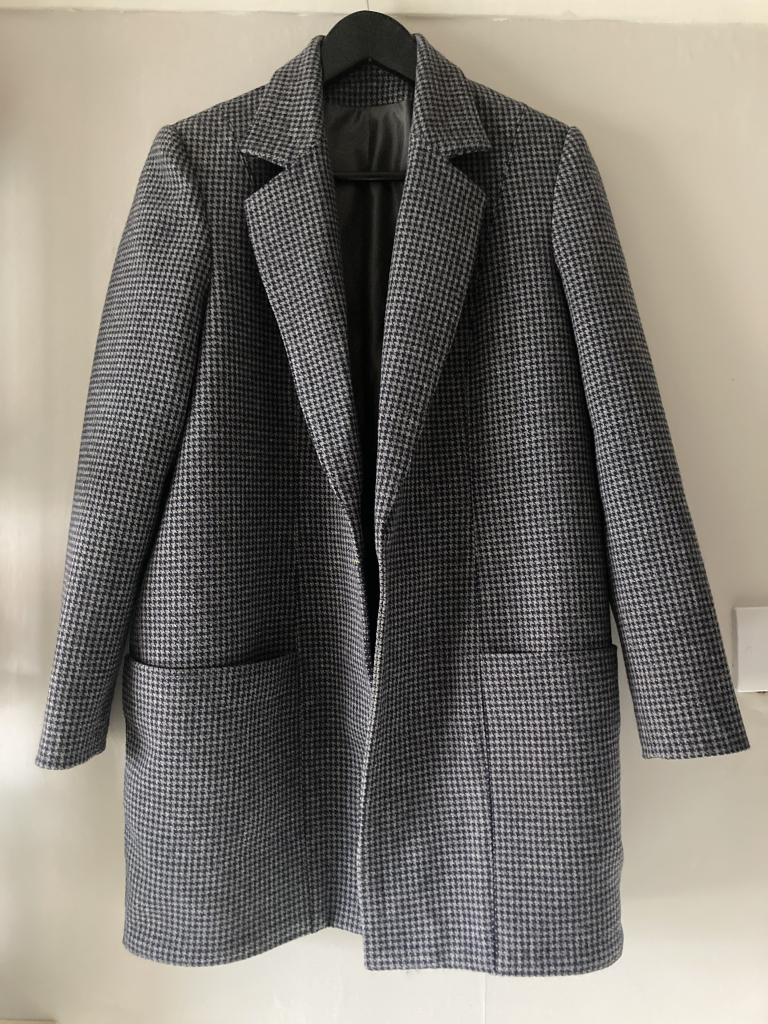 The houndstooth coat (grey and dark navy check) hanging up. It doesn’t have a fastening, yet, at the front. It doesn’t exactly need one, being so generously sized it hangs closed of its own accord.