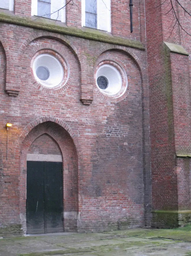 An old red brick building with 2 white round windows and a door under an arch