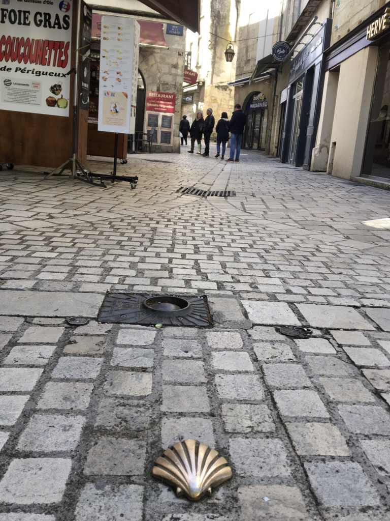 a gold coloured scallop shell in the foreground of a cobbled street