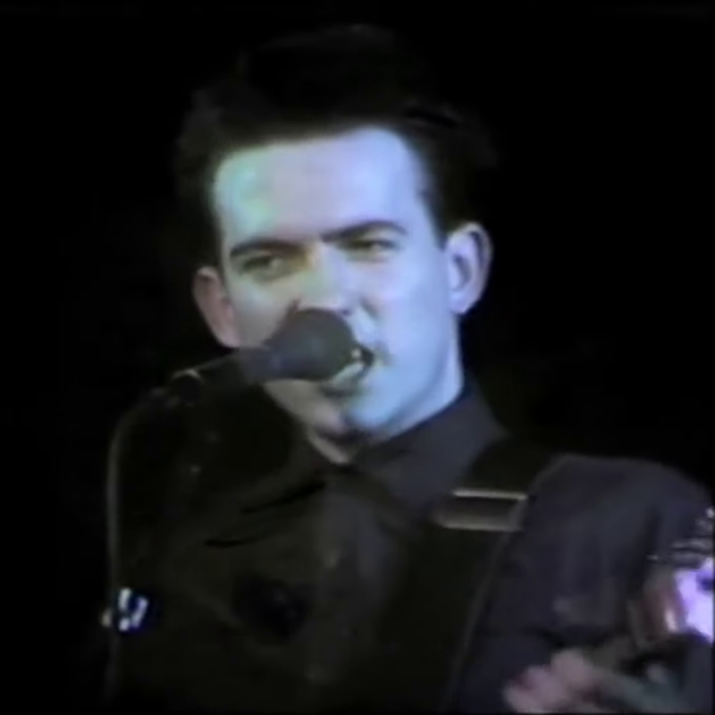 Robert Smith of The Cure singing into a microphone on a small stage in New York, 1980