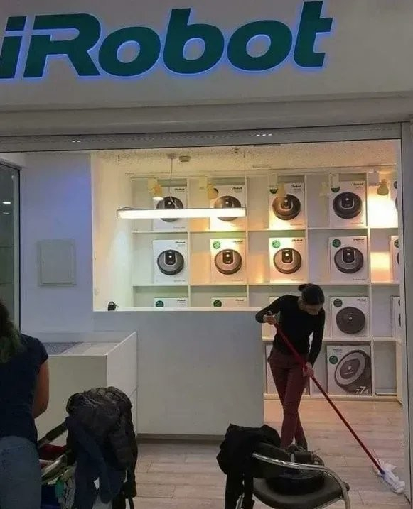 Woman using a broom to sweep up in a store that sells cleaning robots.
