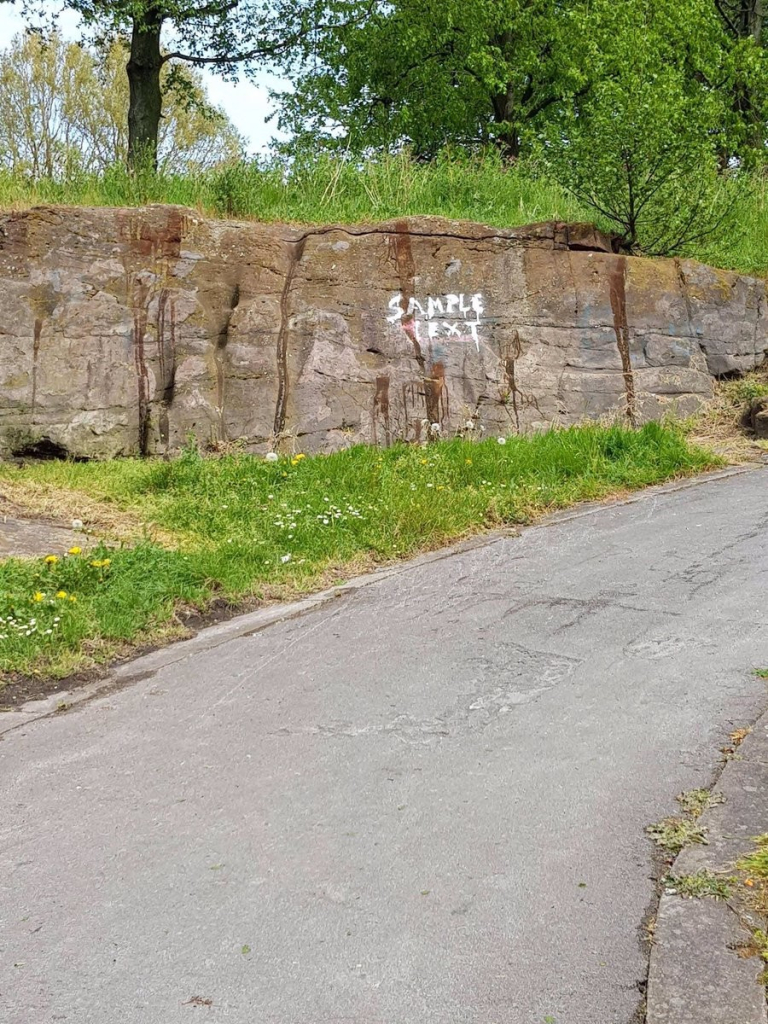 low cliff next to a road with a bit of graffiti that says: "sample text"