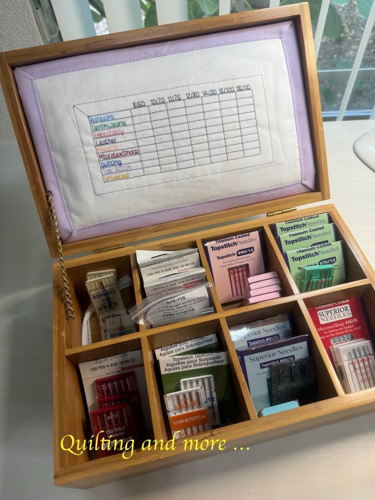 A wooden box with hinged lid. The box is divided into eight small sections, intended for tea bags, but it is full of packages of needles. The lid has a sort of large pin cushion custom fitted into it, marked with a grid for various types and sizes of partially-used needles.