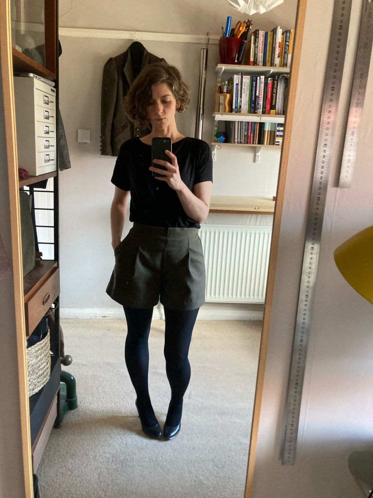 Me wearing homemade, dark-green, pleated shirts, with black tights, shoes and tshirt.