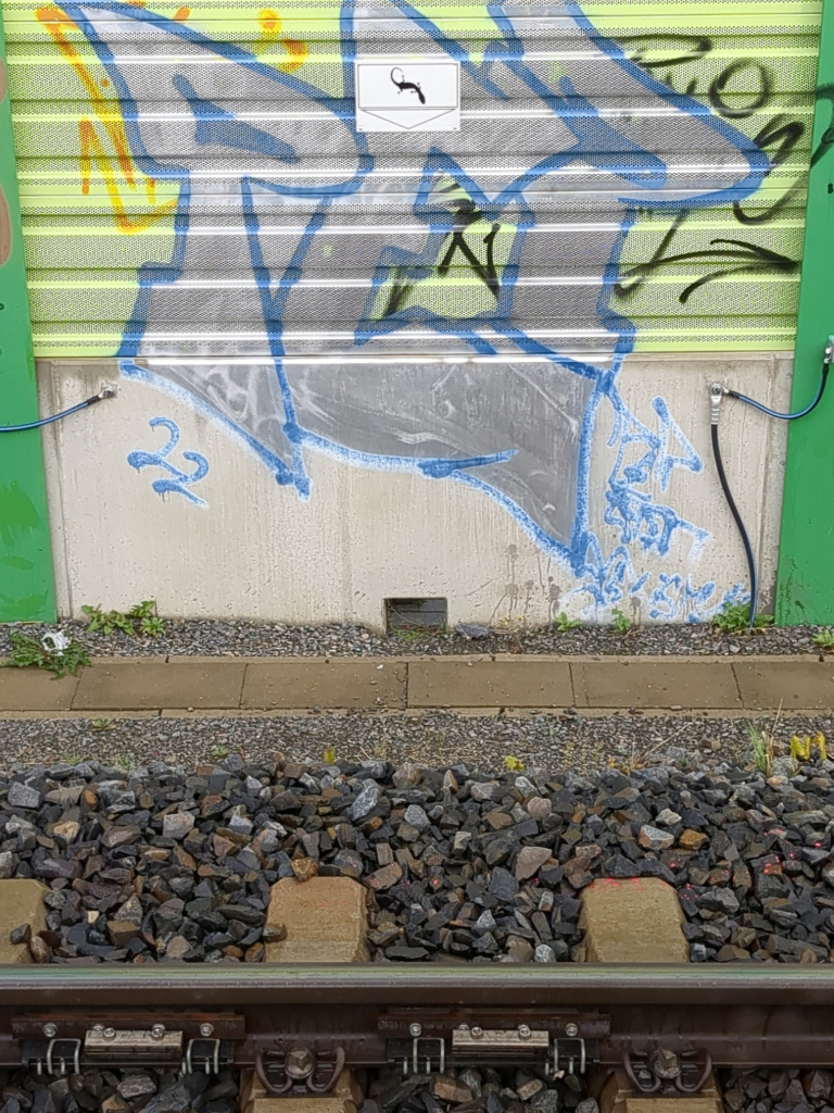 Small opening in block of concrete by railway, with sign above with a lizard logo.