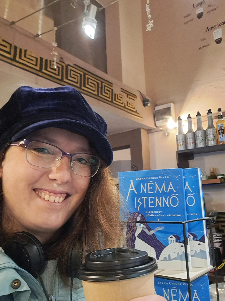 Selfie with The Silent Goddess book (in Hungarian) sold at the café, and a to-go cup of latte. 