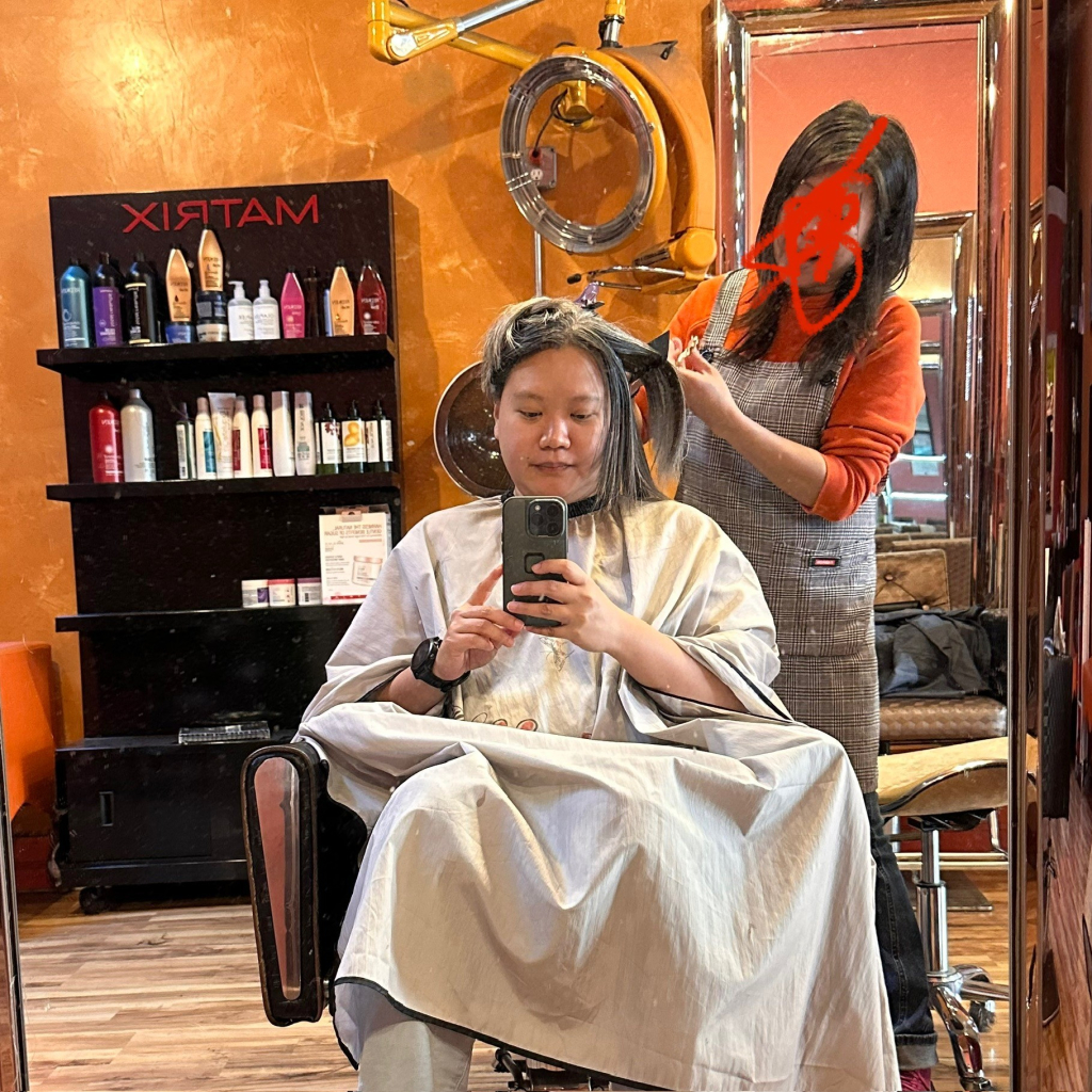 A photo of a person getting a haircut while a Chinese hairstylist tells her a story 