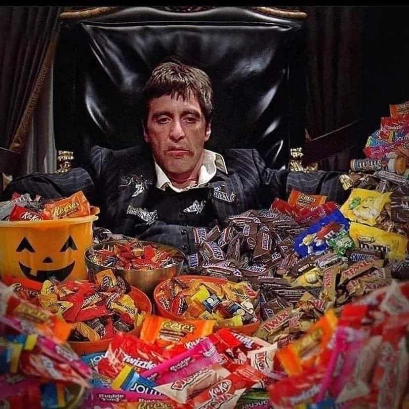 Tony Montana, looking evil and disgusted with himself, with chocolate stains on his face and surrounded by halloween candy