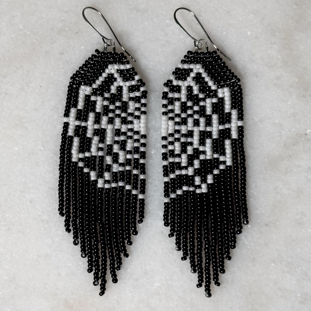 A pair of black and white beaded spiderweb fringe earrings on a marble background