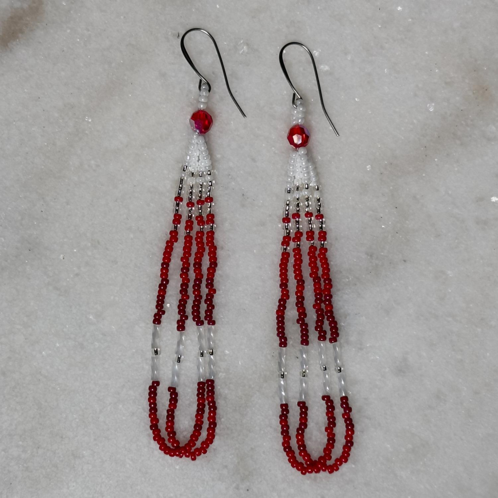 A pair of white and red beaded loop earrings on a marble background