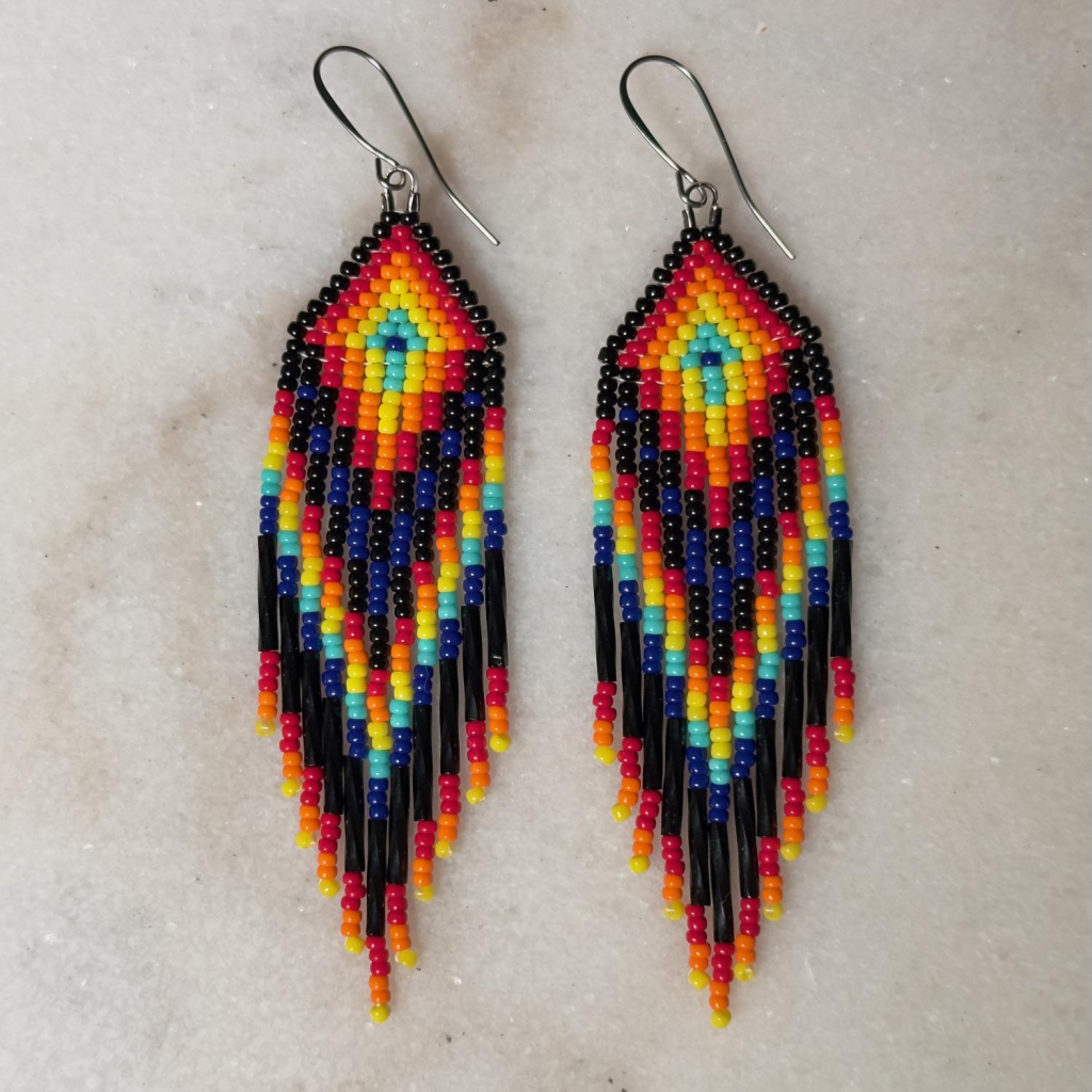 A pair of black, yellow, orange, red, and blue beaded fringe earrings on a marble background