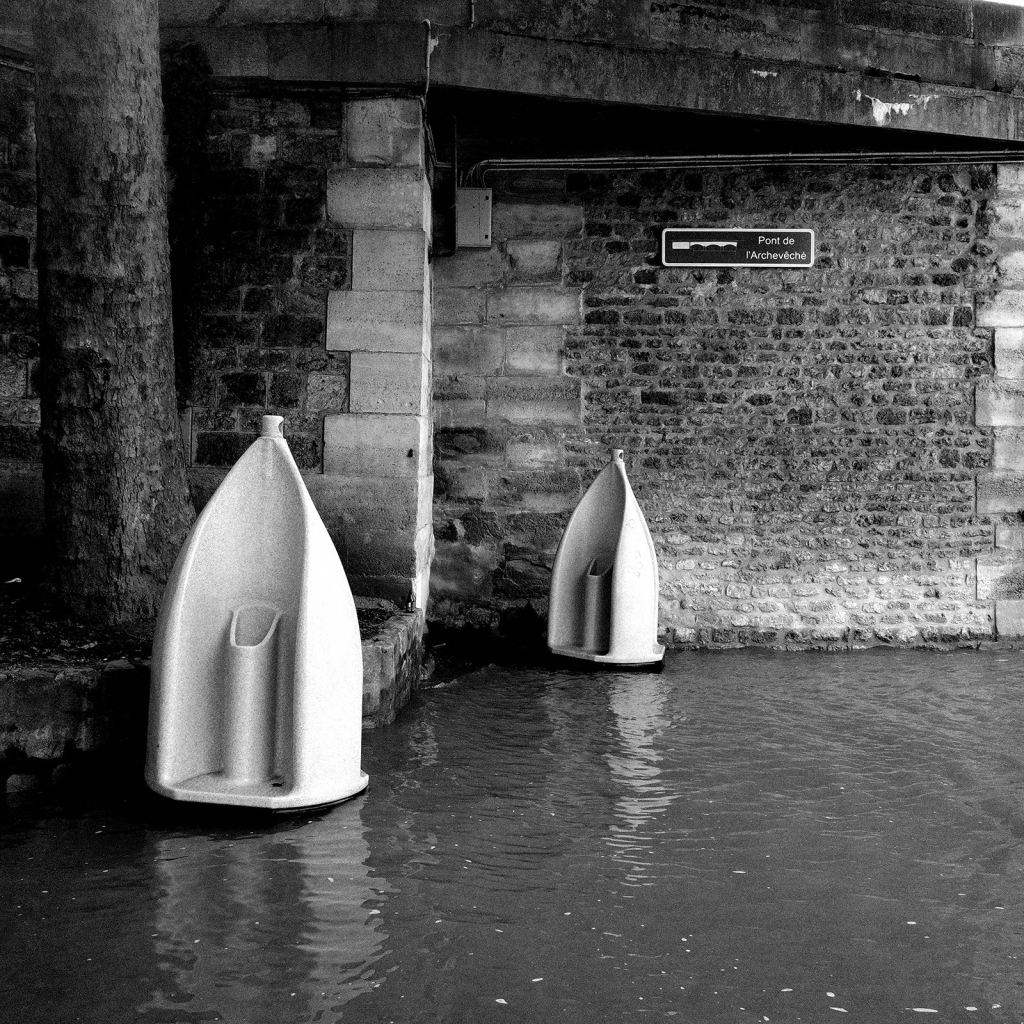 Photo de deux urinoirs installés près du pont de l'Archévêché qui, en raison de la montée de la Seine et son débordement sur le quai, semblent flotter.