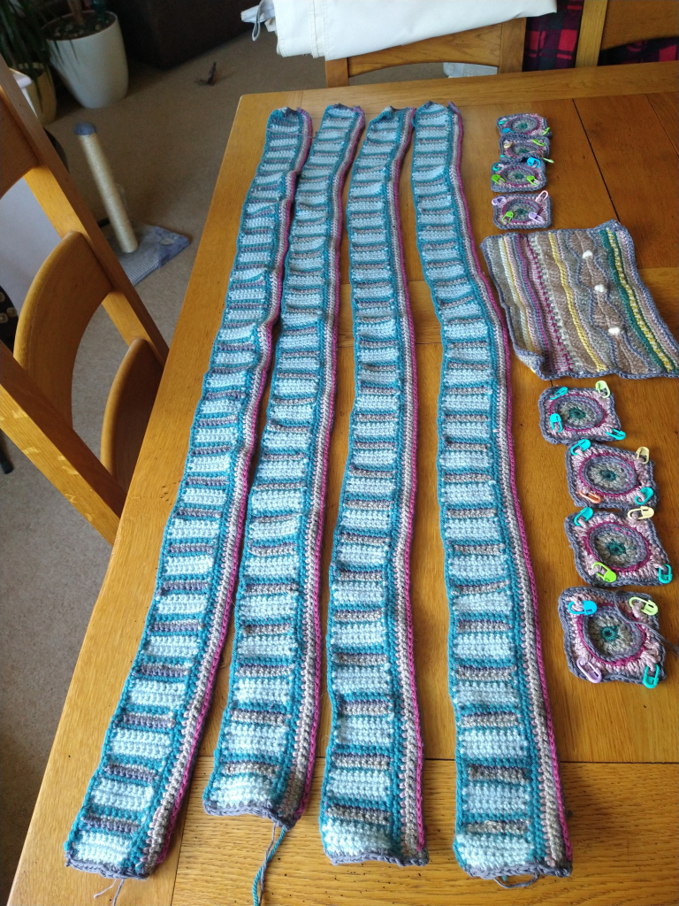 Four long edging pieces of crochet, in blue and grey, with a wine coloured edge, eight small crochet squares to the right and one rectangular piece 