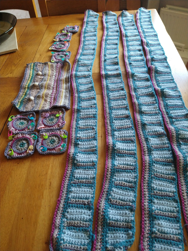 Four long edging pieces of crochet, in blue and grey, with a wine coloured edge, eight small crochet squares to the left and one rectangular piece, which has a wave pattern and bobble stitches and beading 