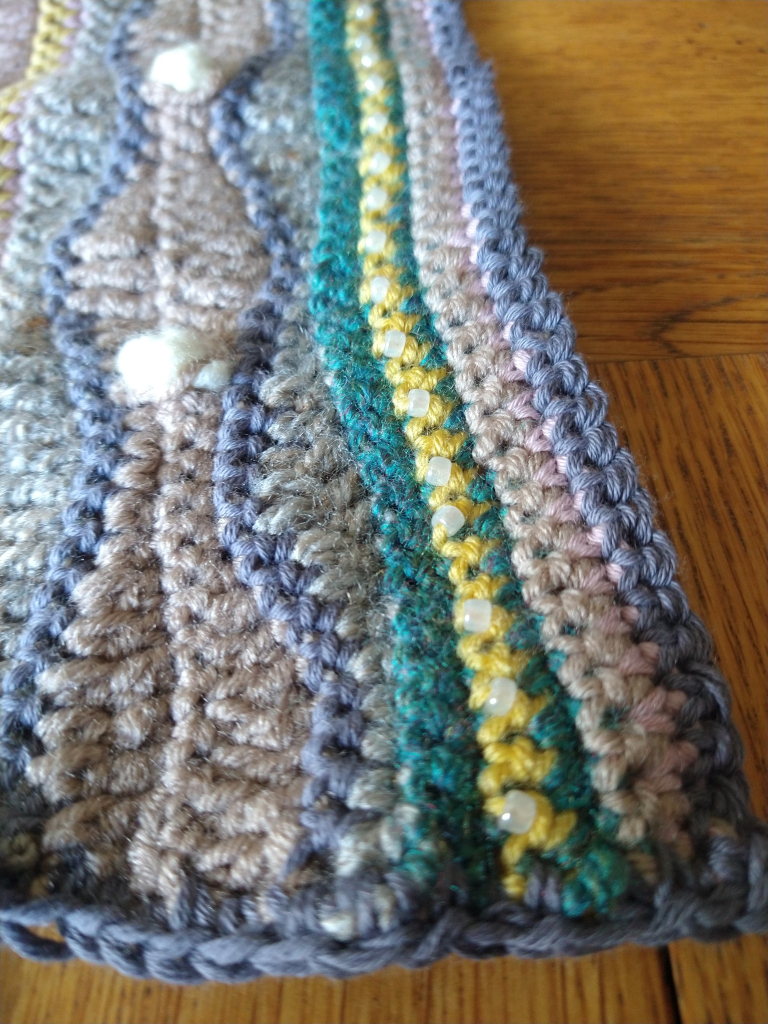 Close up of rectangular crochet piece, which has a wave pattern,  bobble stitches and beading 