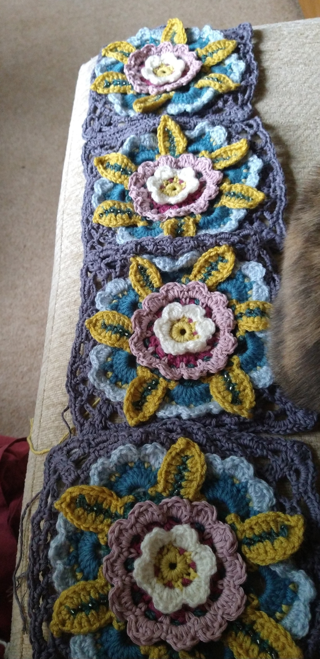 A line of four legacy motif crochet squares. It's a multi coloured flower in a grey lacy square 