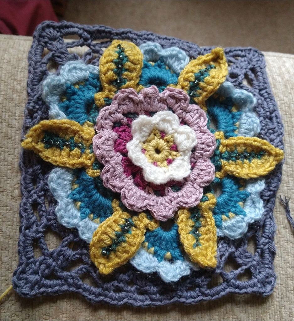 A  Legacy motif crochet squares. It's a multi coloured flower in a grey lacy square 