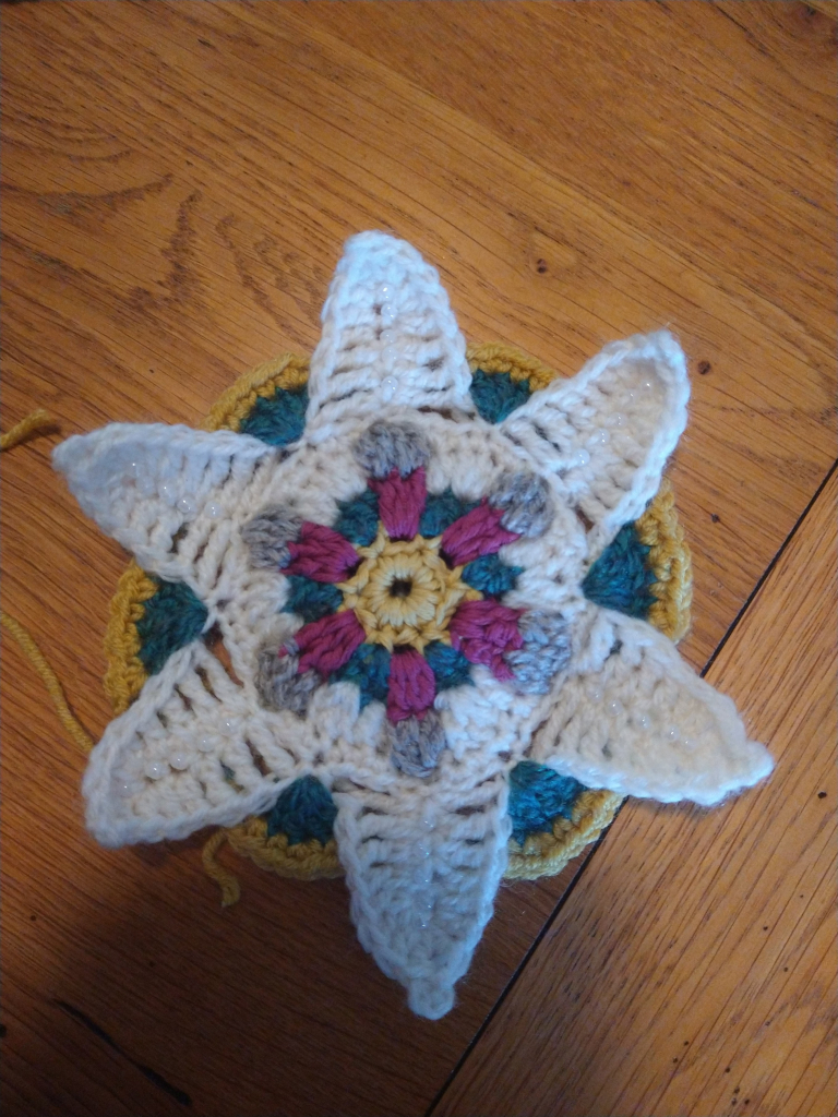 Virginia crochet motif flower, with yellow and pink centre white beaded petals, and green and yellow circular background 