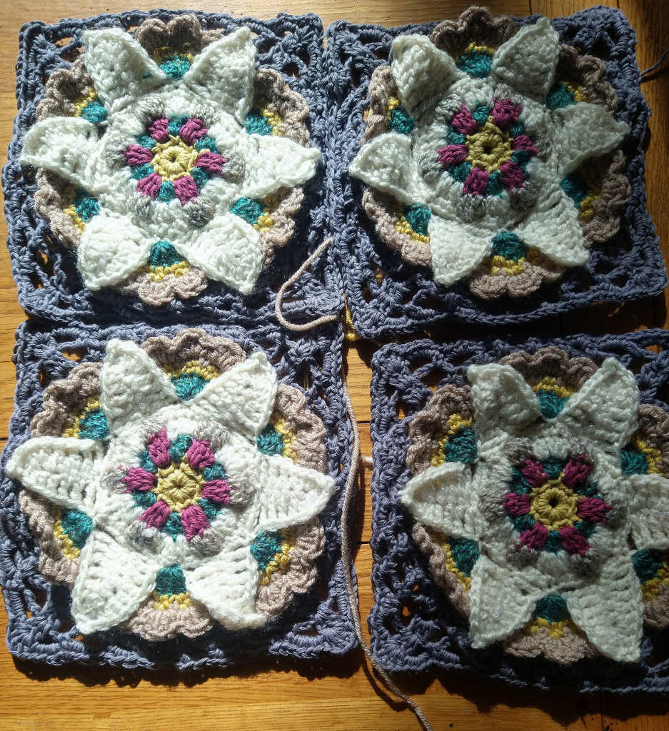 Four Virginia crochet motif, a flower centre with white petals and a lacy grey border 