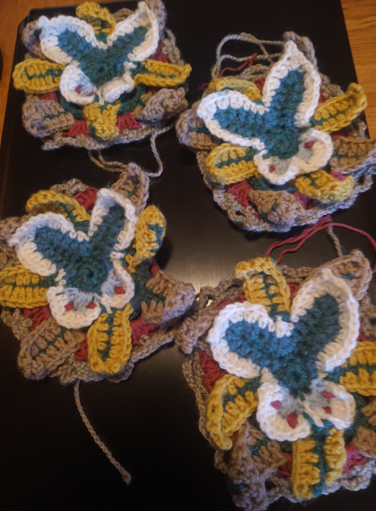 Four Vanessa crochet motifs looking like a butterflies sitting on flowers 