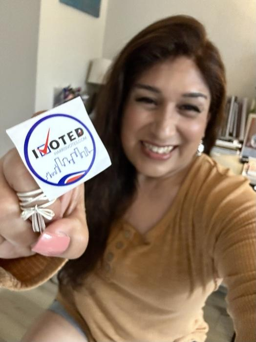 a trans femme Latine enby woman holding her “I voted” sticker