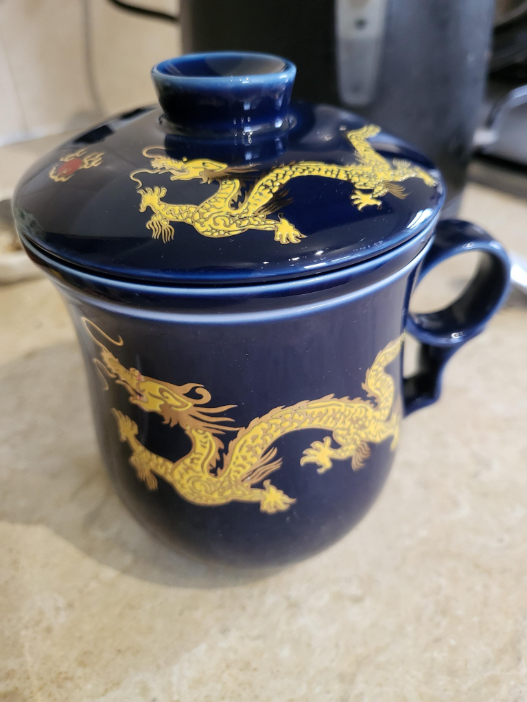 A blue cup with a golden dragon on the cup and on the lid. It's a loose leaf tea infuser, hence the lid. 