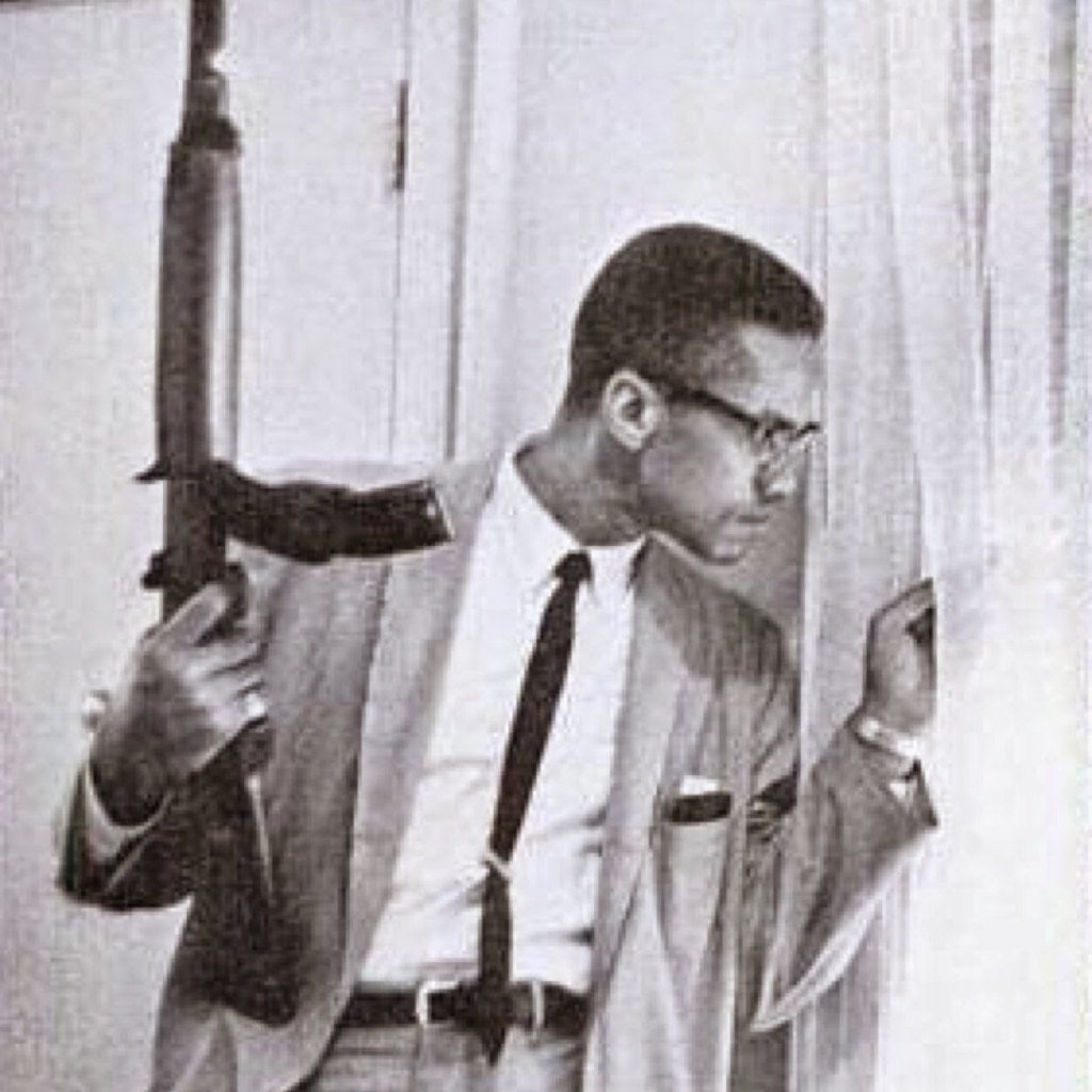 Al-Hajj Malik Al-Shabazz holding a rifle and peeking through window curtains