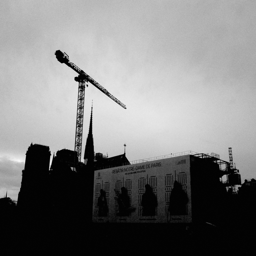 Photo du chantier de Notre-Dame-de-Paris, qui montre une grue tournée au dessus de la nef, et la flèche reconstruite. Devant les bungalows du chantier.