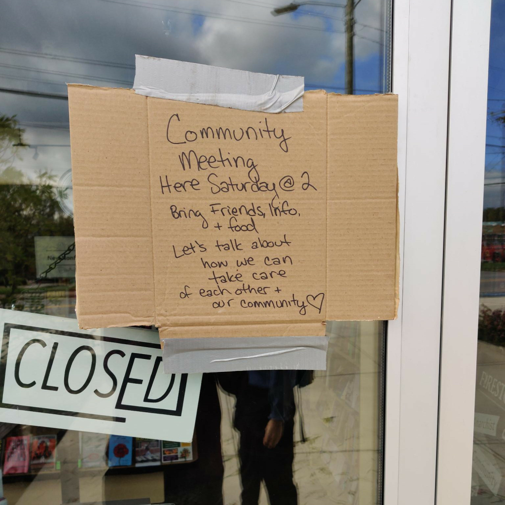 A photo of a handwritten message on cardboard duct taped to the door of Firestorm Books. Through the glass, a closed sign is visible.