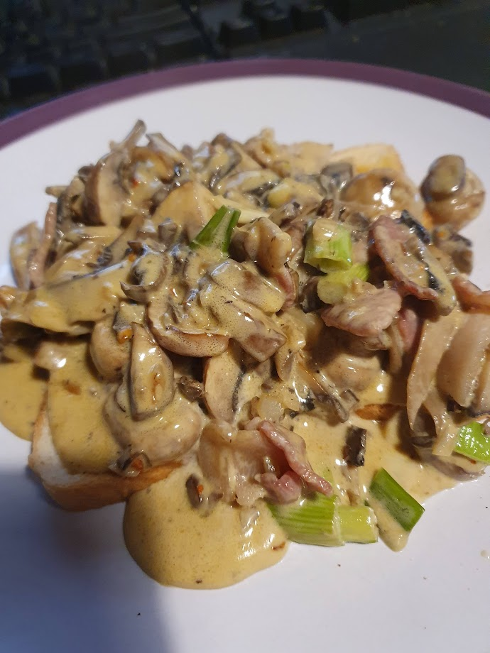 A white plate with purple rim. Creamy garlic mushrooms on toast. 