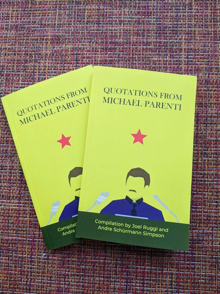 A photo of two copies of "Quotations From Michael Parenti" a compilation by Joel Ruggi and Andre Schürmann Simpson. The cover is yellow and it shows an abstract visual representation of Michael Parenti on the cover from his iconic speeches. The drawing of him has a blue collared shirt and shows his hair and mustache as well as two microphones pointing towards him, one with tape around it. there is a red star in the center of the cover and a green bar at the bottom. The title is stylized in all capital letters and sits at the top. The name of the compilers are at the bottom in yellow text on the green bar. the books overlap and rest on top of a woven fabric.