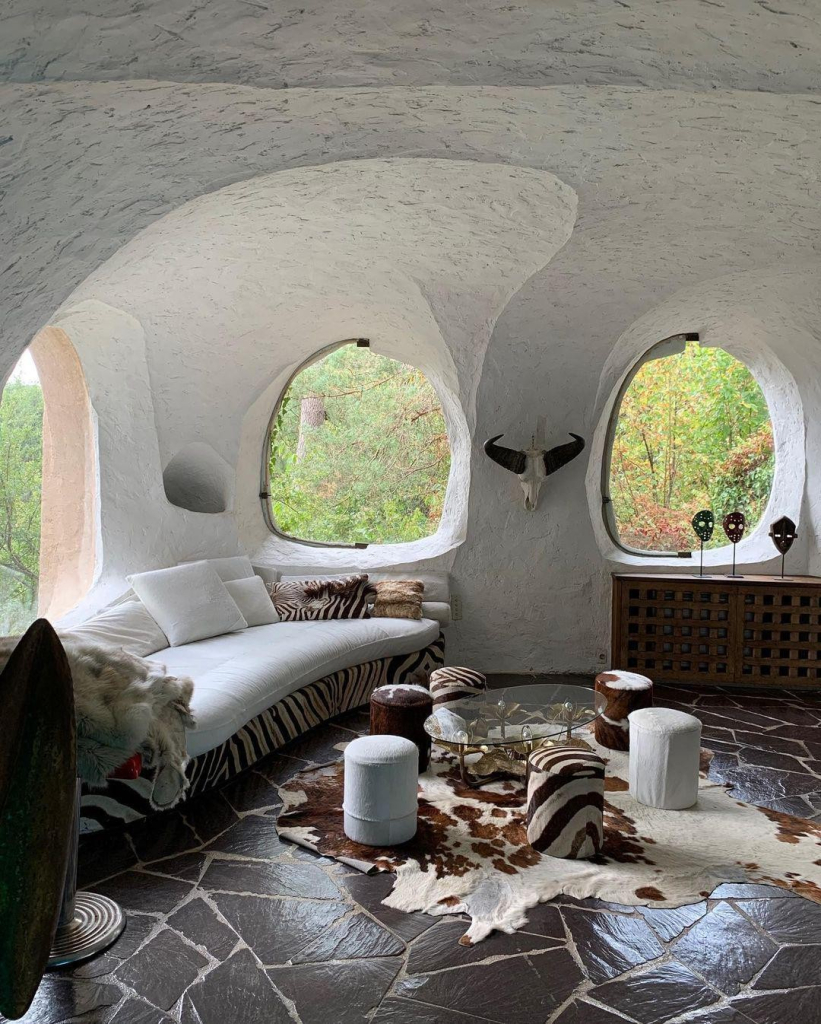 Domestic interior with curving white walls and round windows, a dark abstract tiled floor, and white and brown furniture