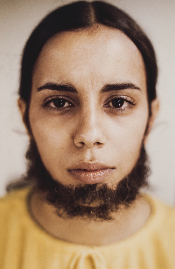 Photo of Mendieta in closeup looking directly at the viewer, with dark hair applied to her chin and jaw in a beard