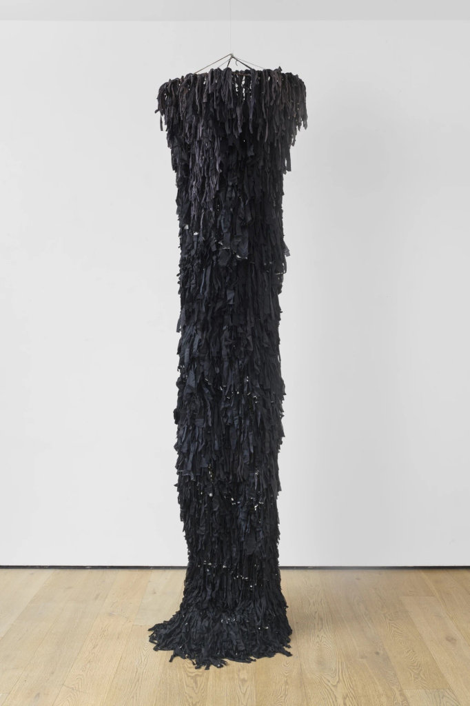 Standing column of overlapping black fabric scraps suspended by wire