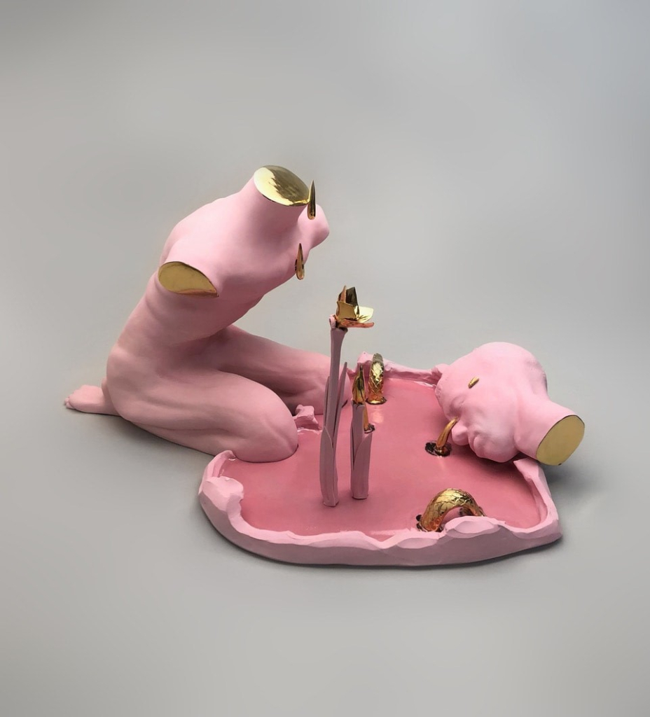 Ceramic sculpture of an armless pink nude body kneeling next to a heart-shaped pink pool, its chopped-off head lying next to it and crying gold 