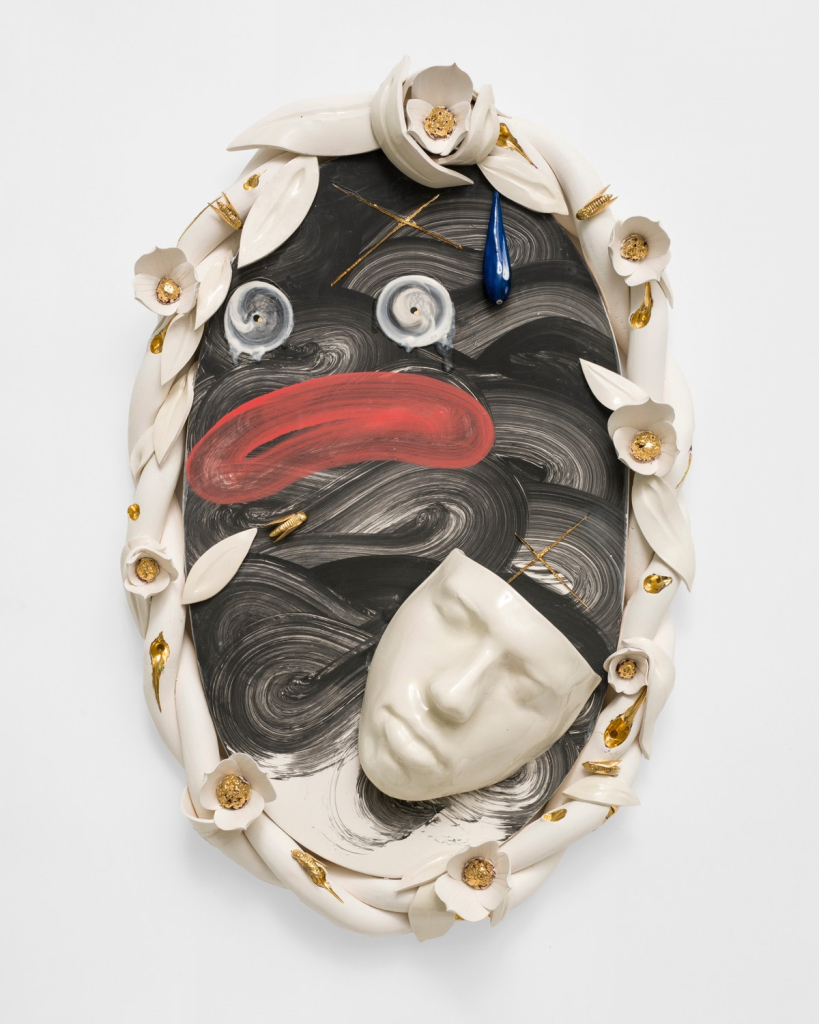 Hanging wall sculpture of an oval floral frame with black swirls painted on the interior and a loose rendering of a Blackface cartoon, overlaid with a 3-d clay mask of a human face in white