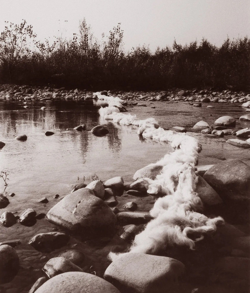 Black and white image of line of cotton fiber laid across a rocky, shallow riverbed