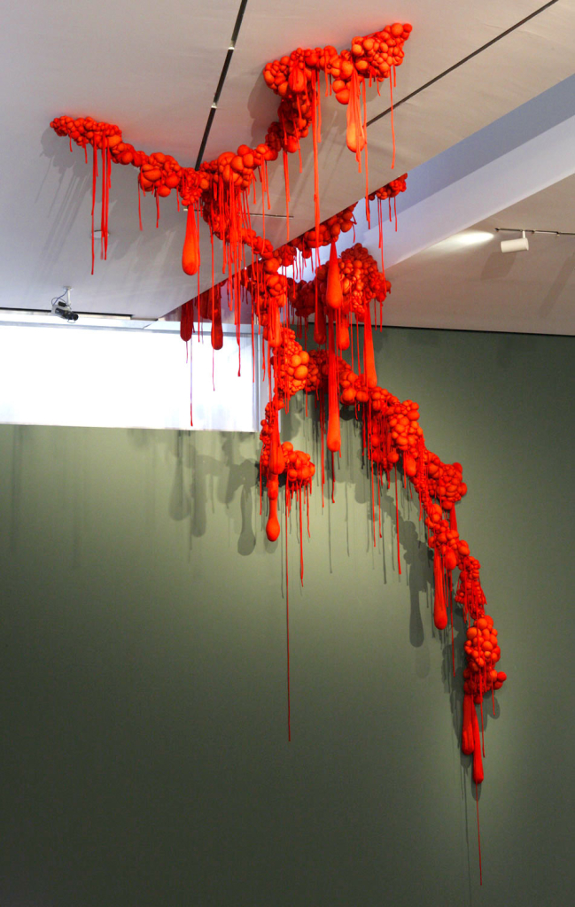 Red, drooping abstract sculpture handing from a white ceiling 