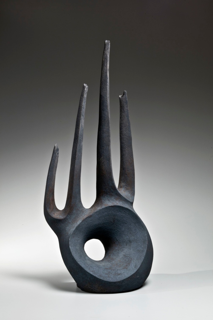 Black abstract sculpture of a circular form with four slender points erupting from the top