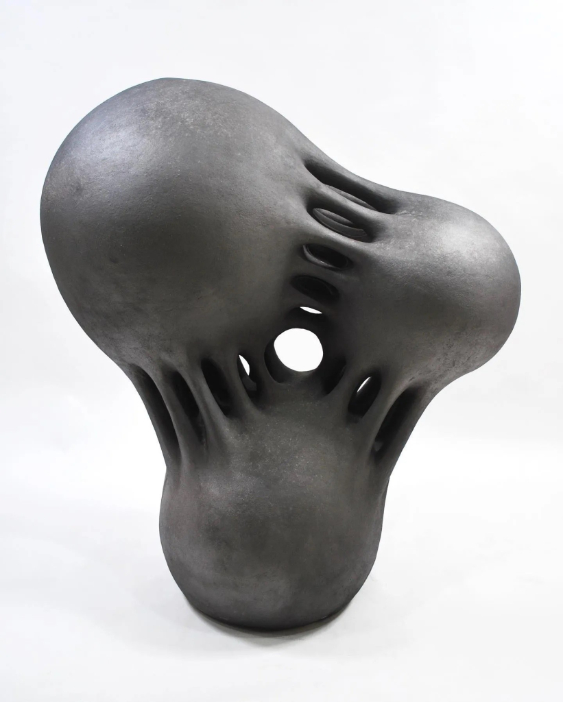 Black abstract sculpture of three balls linked by stretched sinewy connections