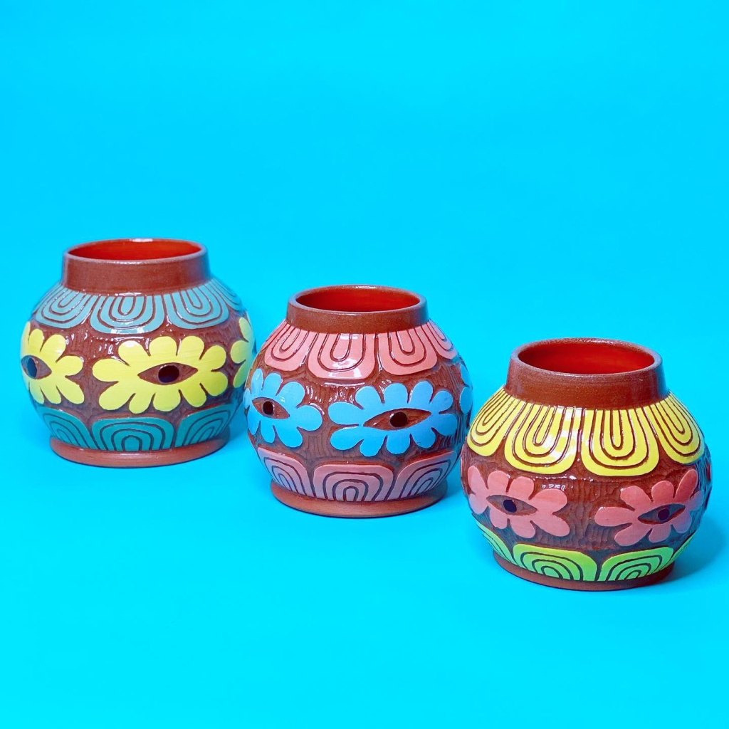 Three small round pots with colorful floral eye designs on red-orange bases